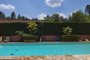 A swimming pool with a stone border, surrounded by neatly trimmed hedges and a row of lounge chairs.
