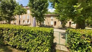 Une cour avec une haie, un bâtiment en pierre et un portail.