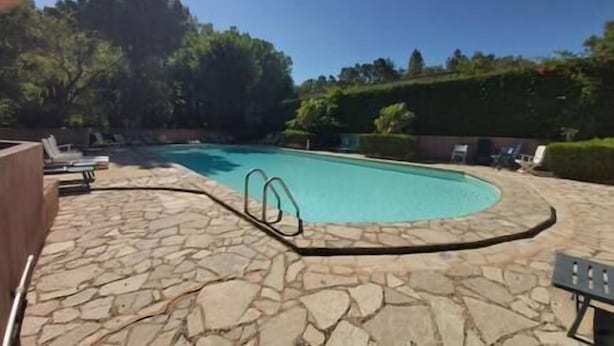 Une piscine dotée d’une terrasse en pierre, entourée de chaises longues et d’une haie.