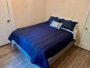Un lit simple avec une couvre-lit et des oreillers bleu foncé, un plancher en bois et une porte blanche.
