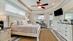 A bedroom with a bed, bedside tables, a desk, a television, and a ceiling fan. - Luxury 4 BR/3BA Waterview Home w/ Pool + Spa with work space (Bradenton)