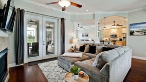 A living room with a sectional sofa, a coffee table with a plant, and a view of the kitchen and dining area through an open door. - Luxury 4 BR/3BA Waterview Home w/ Pool + Spa with work space (Bradenton)