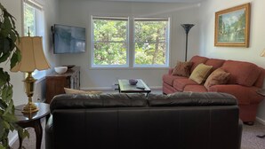 Een woonkamer met een rode bank, een zwarte leren bank, een kleine tafel met een kom, een lamp en een schilderij aan de muur.