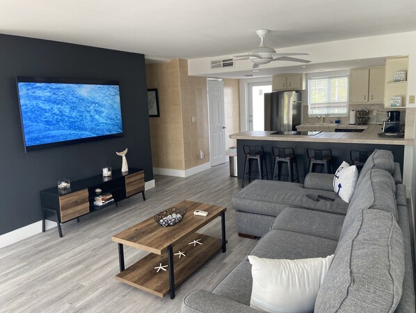 A modern living room with a grey sofa, a wooden coffee table, and a TV mounted on a dark wall. - Fun For All! Key Largo 3/3 Townhome Oceanside Resort (Key Largo)