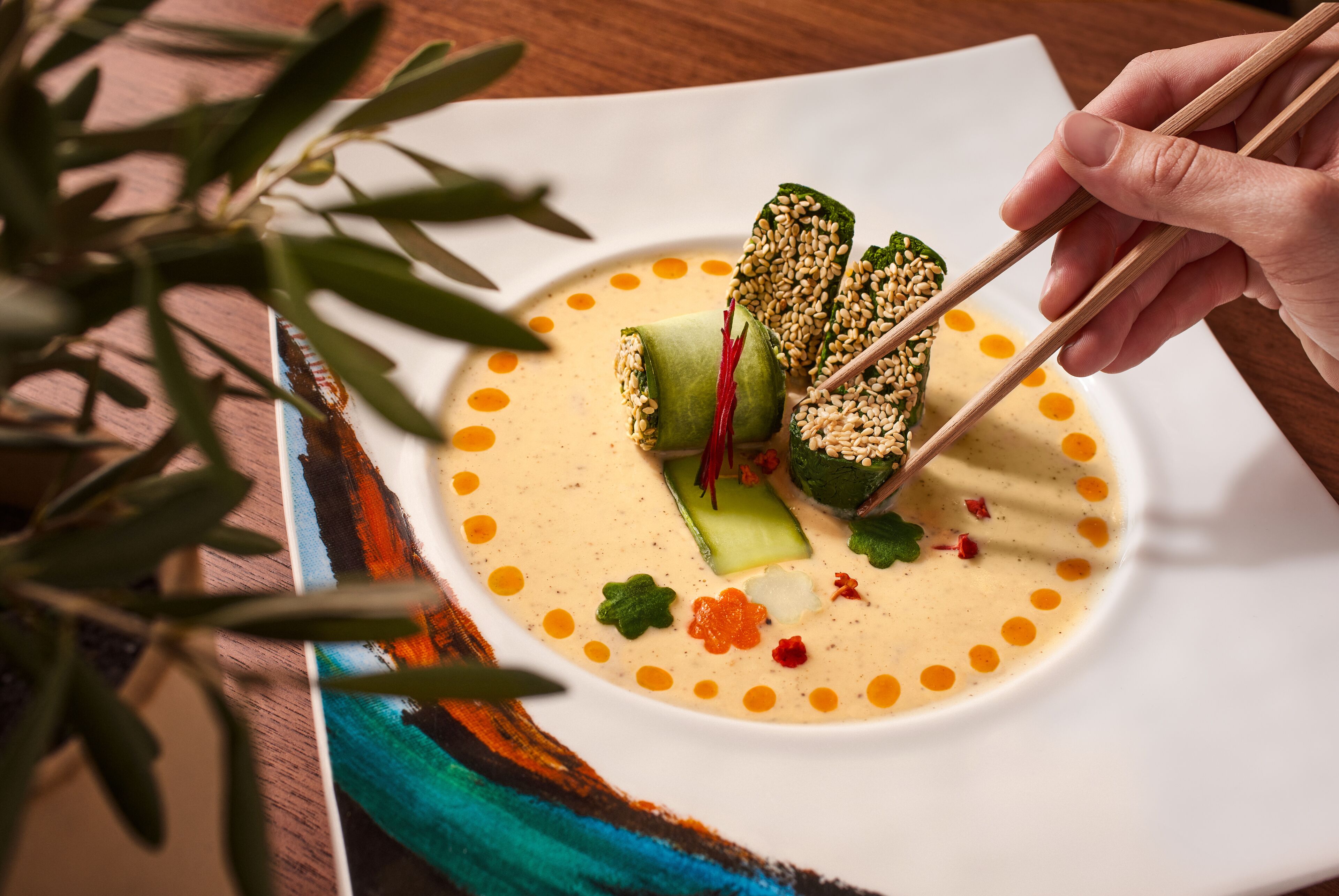 A plate of food with chopsticks, a plant, and a colorful tablecloth.