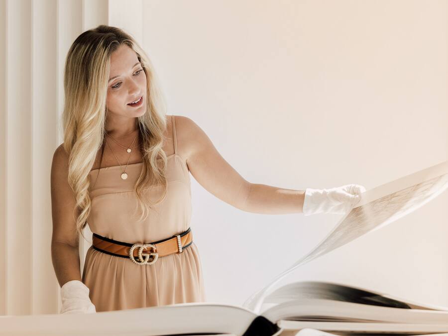 Une personne se tient près d’un piano, vêtue d’une robe beige et de gants blancs.