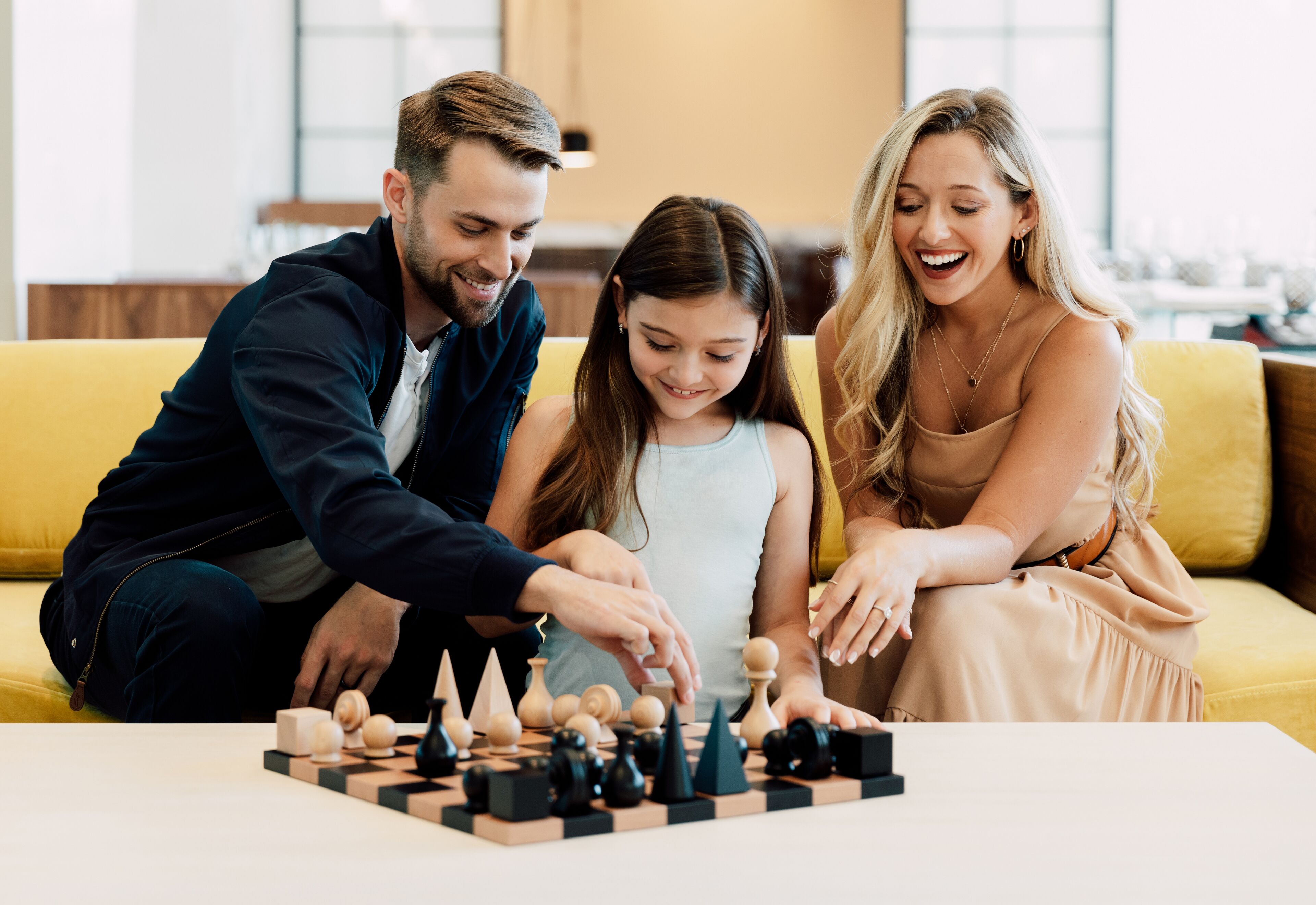 A family playing chess on a yellow couch in a well-lit room with a modern interior.