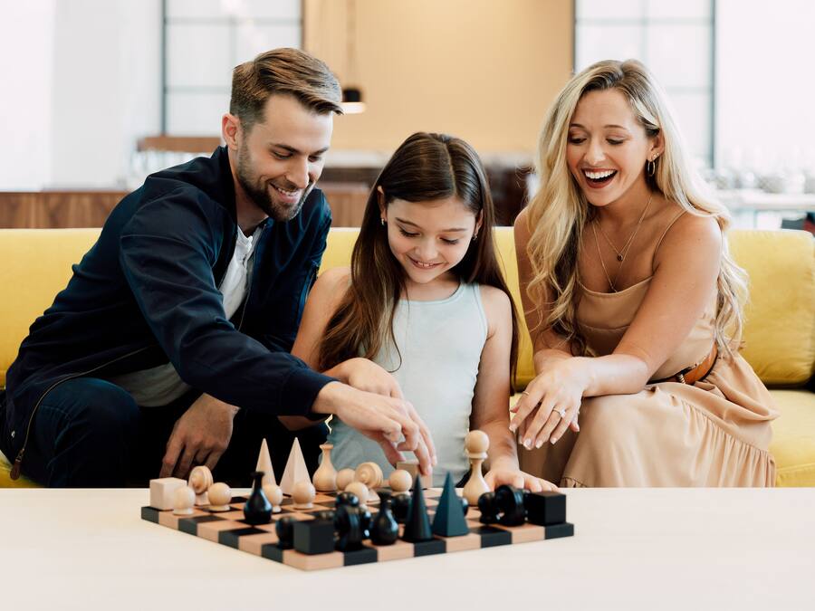 A family playing chess on a yellow couch in a well-lit room with a modern interior.