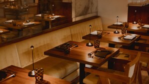 A restaurant interior with wooden tables and chairs, a marble wall, and a seating area with a cushioned bench. - ette hotel (Kissimmee)