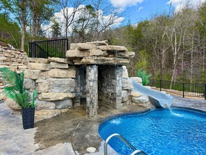 A swimming pool with a stone waterfall and a slide, surrounded by a stone wall and a metal fence. - Private Retreat For You w/HEATED Pool, Private Dock,  Activity gym, 100 acres! (Galena)