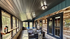 A cozy log cabin with a ping pong table, wicker furniture, and large windows offering views of the surrounding forest. - Private Retreat For You w/HEATED Pool, Private Dock,  Activity gym, 100 acres! (Galena)