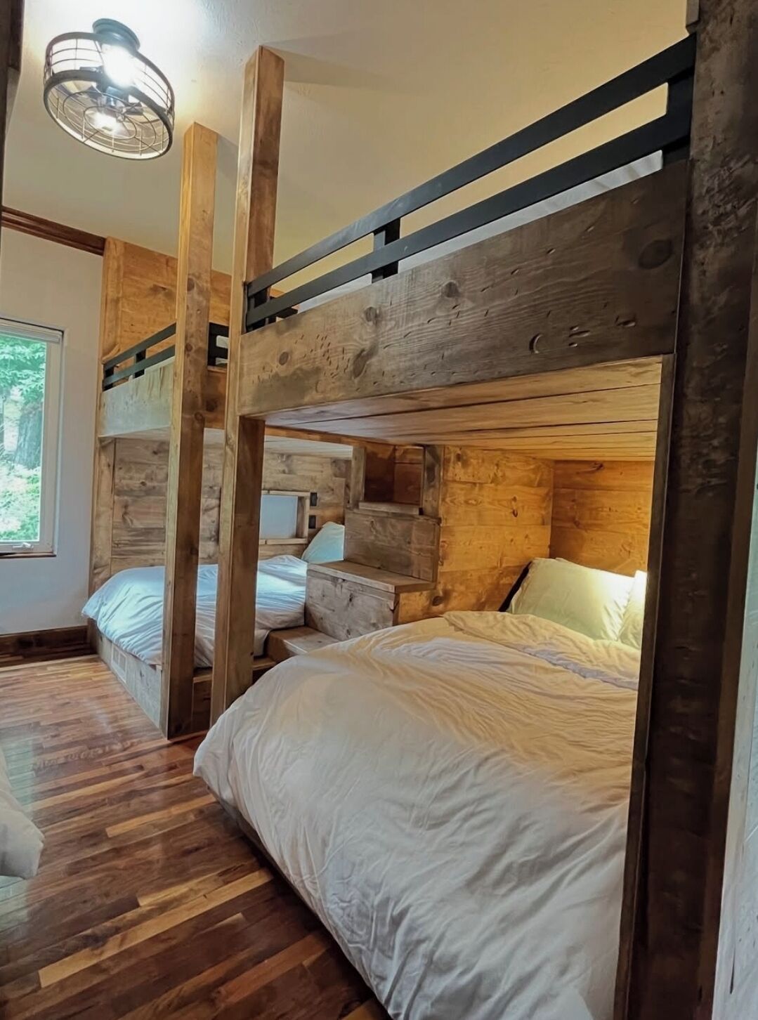 Une chambre rustique avec des lits superposés en bois, un plancher en bois et une fenêtre donnant sur un paysage verdoyant.