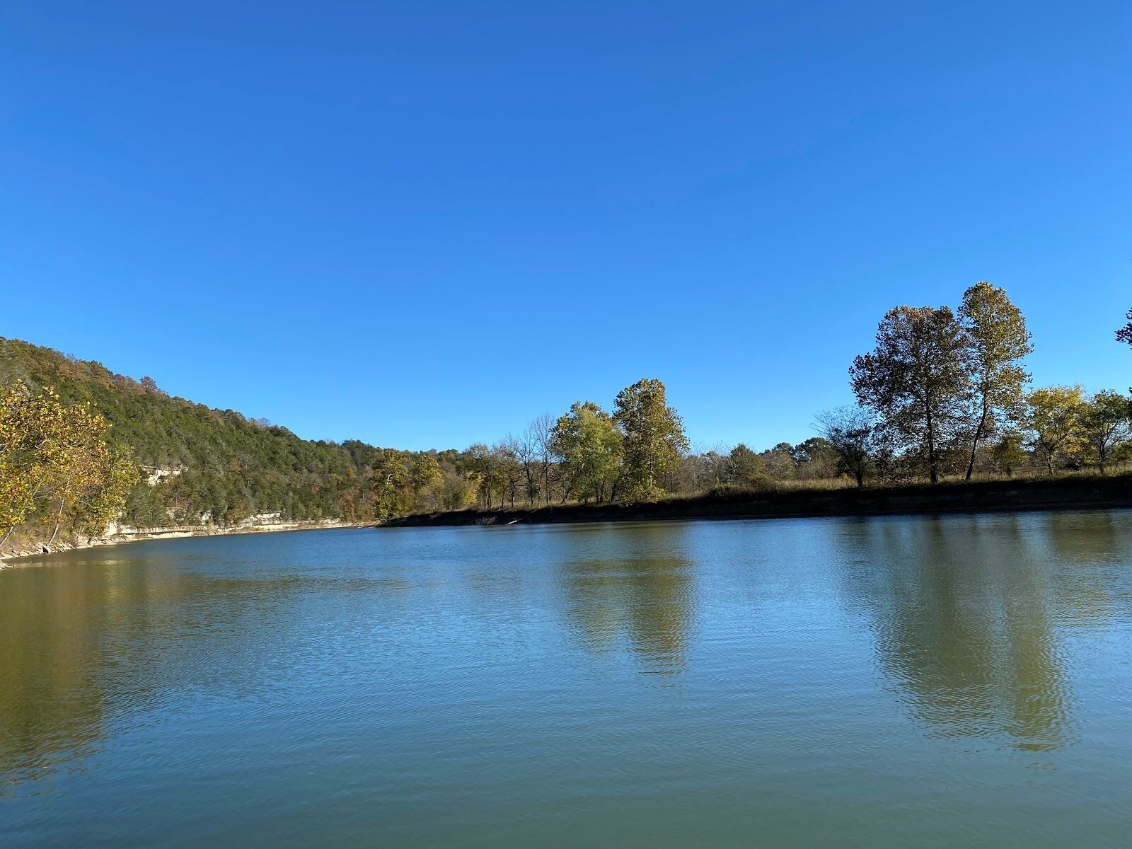 A calm lake with a forested hillside and a clear blue sky.