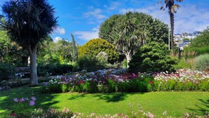 A lush garden with diverse flora, a bench, and a clear blue sky.