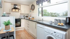 A compact kitchen with white cabinets, a dishwasher, and a window with a view of trees.