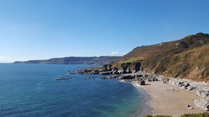 A coastal landscape with rocky cliffs, a sandy beach, and clear blue water.