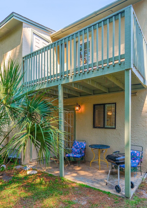 A covered patio with a railing, two chairs, a small table, and a grill.