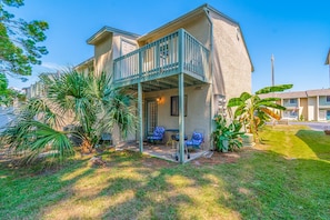 A two-story building with a balcony, outdoor seating, and tropical plants.