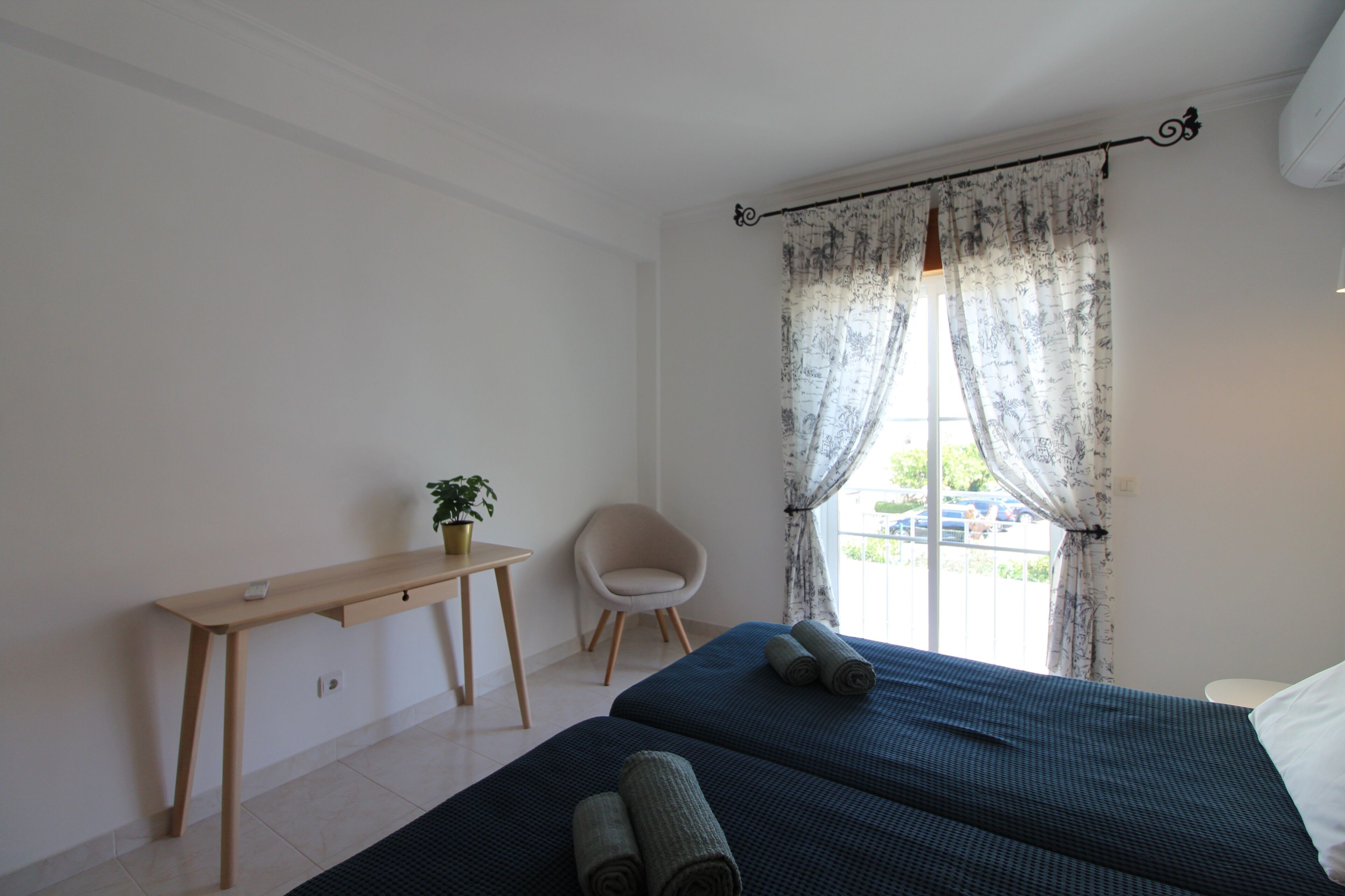 A bedroom with a bed, a desk, a chair, and a window with curtains.
