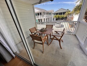 A covered patio with a wooden table and chairs, a small decorative plant, and a view of neighboring houses. - Elevator, Pets Welcome >5 min walk to Beach & Dining! (Tybee Island)