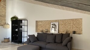 Un salon avec un canapé gris, un meuble noir et un mur en pierre.