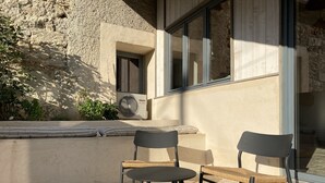 Un espace extérieur aménagé avec deux chaises et une petite table, un mur en pierre et un appareil de climatisation.