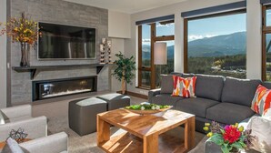 Una sala moderna con chimenea, un televisor de pantalla plana grande, un sofá y vistas a las montañas.