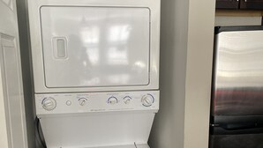 Uma máquina de lavar e secar compacta numa cozinha com armários de madeira escura.