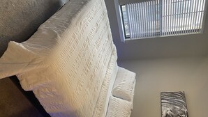 Quarto com uma cama, janela com persianas e um quadro pendurado na parede.