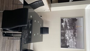 Uma zona de refeições moderna com uma mesa e cadeiras pretas, uma janela ampla com vista para a cidade e uma parede branca.