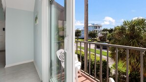 A balcony with a view of a residential area, including a house and palm trees.