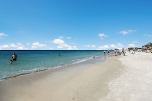 A beach with clear blue water, people swimming and walking along the shore, and beachgoers relaxing on the sand. - 2 Bedroom Townhouse for Unforgettable Vacations! (Holmes Beach)