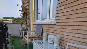 Een klein terras buiten met een rieten bank, een eettafel en potplanten.