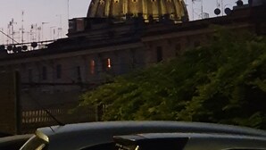 Een grote, verlichte koepelstructuur met een torenspits, omringd door gebouwen en antennes.