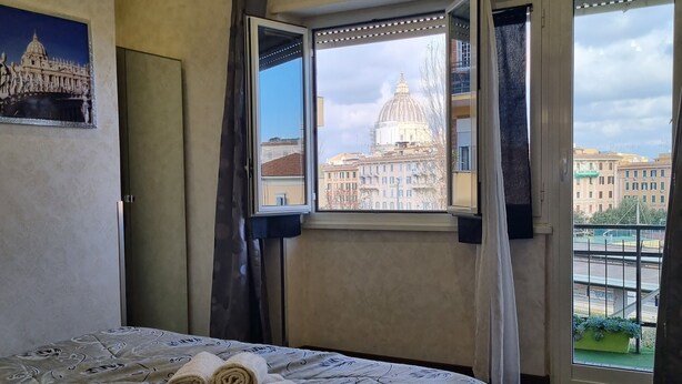 Hotelkamer met een groot bed, uitzicht op een stadslandschap door een raam en een kroonluchter.