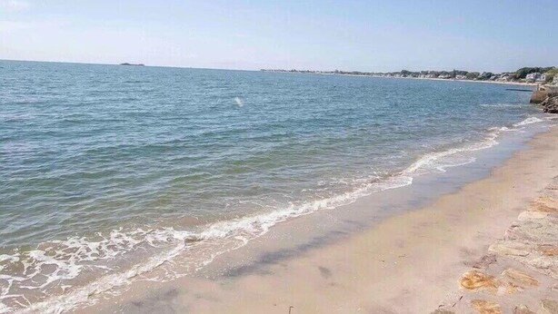 Une plage avec une eau d’un bleu limpide, un rivage sablonneux et des affleurements rocheux.