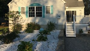 Une maison à deux étages avec un porche couvert, une cour avant avec du gravier et des plantes, et une cheminée.