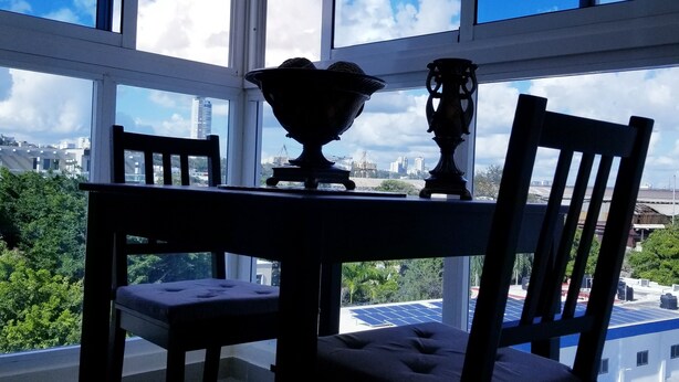 A dining area with a table and chairs, a decorative bowl, and a view of a cityscape through large windows. - Wonderful Apartment Santodomingo (Santo Domingo Este)