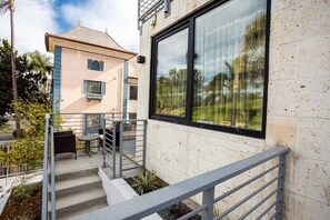 Un bâtiment moderne doté d’une grande fenêtre, d’un escalier avec une rampe en métal et d’un petit espace extérieur aménagé avec une table et des chaises.