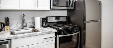 A modern kitchen with stainless steel appliances, white cabinets, and a marble countertop.