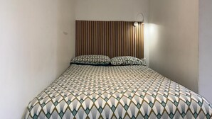 Una habitación pequeña con una cama individual, cabecera de listones y colcha estampada.
