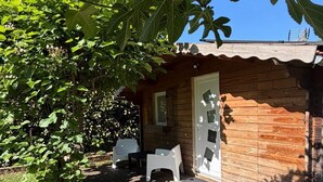 Una cabaña de madera con un porche, dos sillas de plástico blancas y una puerta.