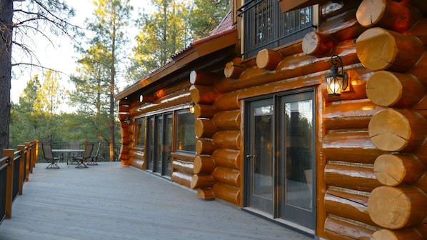Eine Blockhütte mit einer Terrasse, Sitzgelegenheiten im Freien und großen Fenstern.