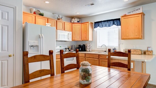 Une cuisine avec des meubles de rangement en bois, un réfrigérateur blanc, un four à micro-ondes et une table à manger avec des chaises.