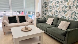 Uma sala de estar com um sofá bege, um sofá verde e uma mesa de centro branca.