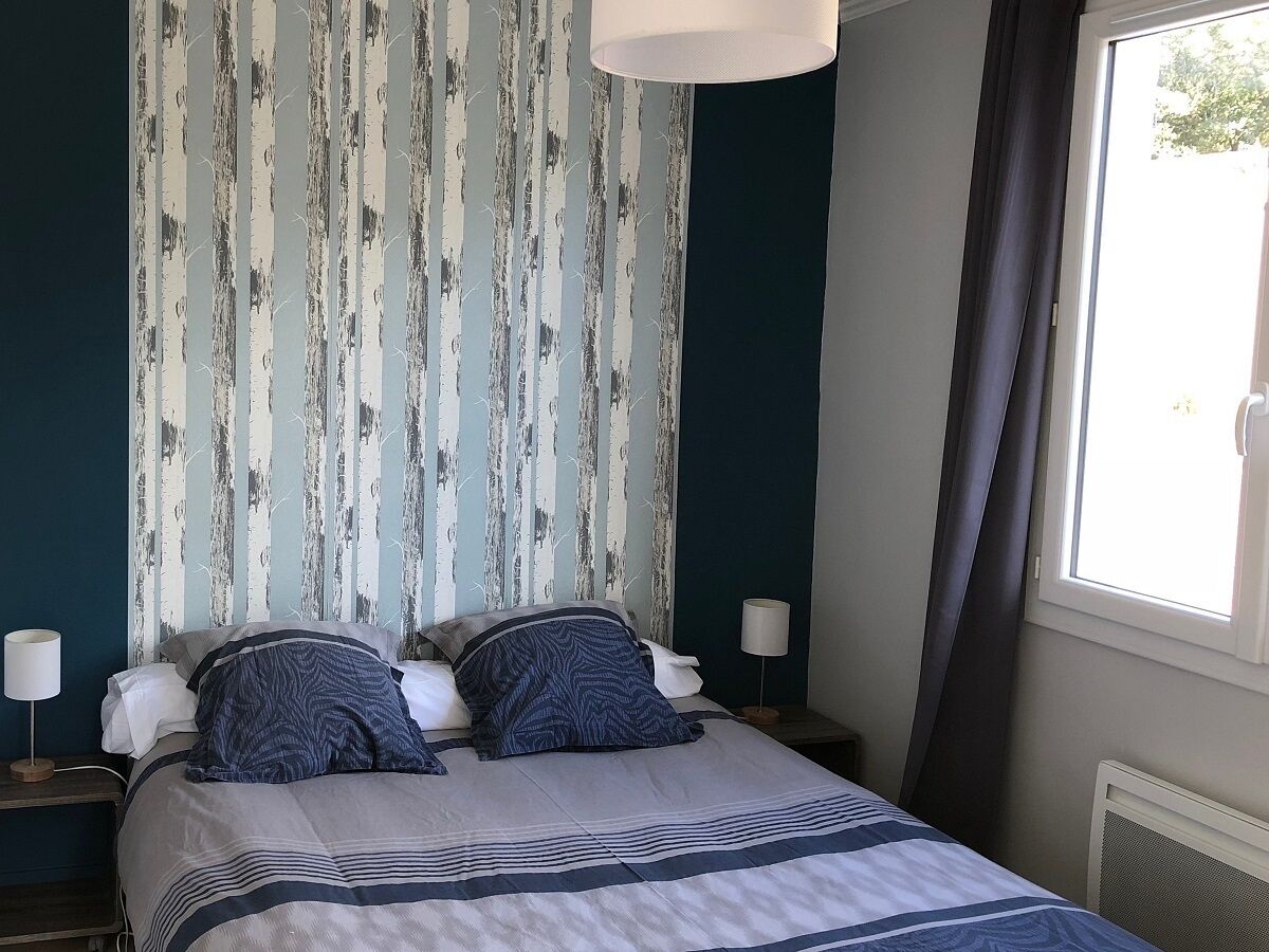 A bedroom with a bed, two bedside lamps, a window with curtains, and a wall with vertical stripes.