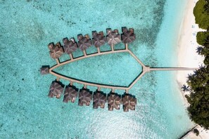 An aerial view of a resort with a unique crescent-shaped pool surrounded by lounge chairs and umbrellas. - Fihalhohi Maldives (Fihalhohi Island)