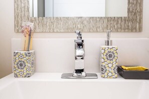 Un lavabo de baño con un grifo moderno, dos dispensadores de jabón estampados y un porta cepillos de dientes.