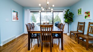 Un comedor con mesa y sillas de madera, una lámpara en el techo y vistas a través de un ventanal grande.