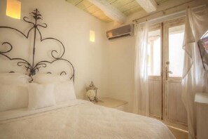 A bedroom with a bed, a decorative wall piece, an air conditioning unit, and a window with curtains. - Splendid Colonial Villa with Rooftop & Jacuzzi (Cartagena)